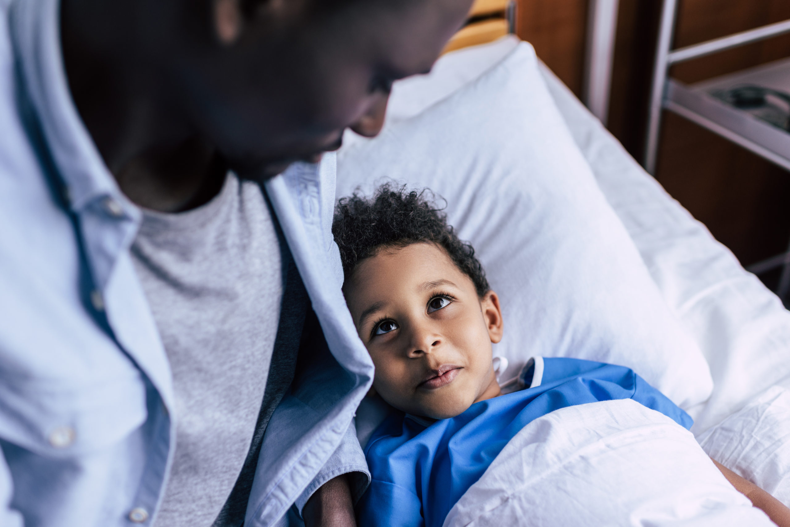 happy boy looking at father while lying in bed in clinic
